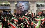 Iranians lift national flags during a ceremony in the capital Tehran, on January 3, 2022, commemorating the second anniversary of the killing in Iraq of top Iranian commander Qassem Soleimani (portrait) and Iraqi commander Abu Mahdi al-Muhandis in a US raid. (Atta Kenare/AFP)