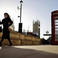 A woman wearing a face covering due to COVID-19 walks past a red telephone box on Whitehall, near the Houses of Parliament in central London, January 20, 2022. (Tolga Akmen/AFP)