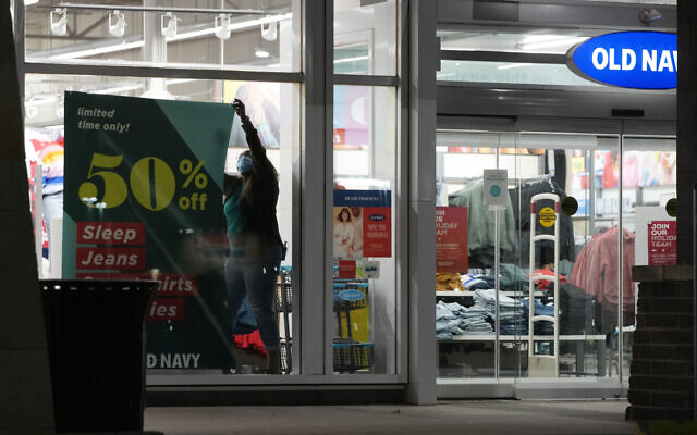 A worker hangs a sign to advertise discounted prices in the front window of an Old Navy store after doors opened at 5 a.m. Friday, Nov. 26, 2021, in Lone Tree, Colo. (AP Photo/David Zalubowski)
