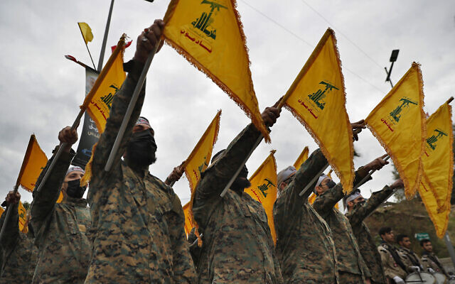 Hezbollah fighters hold their group's flag as they stand in front of a statue of Iranian General Qassem Soleimani and swear their oath of allegiance to him, during a ceremony to mark the second anniversary of his assassination, in the southern suburb of Beirut, Lebanon, on Tuesday, January 4, 2022. (AP Photo/Hussein Malla)