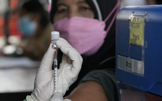 A woman looks on, as a health worker prepares to administer a booster shot of Pfizer COVID-19 vaccine at a community health center in Jakarta, Indonesia, on January 12, 2022. (AP Photo/ Dita Alangkara)