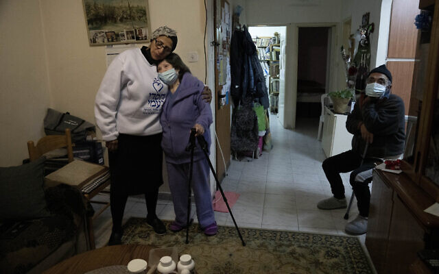 Tshuva Kabra, left, director of the national welfare system at the Chasdei Naomi charity, embraces Holocaust survivor Freida Rovenchim, in her family apartment in Jerusalem, January 26, 2022 (AP Photo/Maya Alleruzzo)