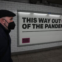 A man wearing a face mask to curb the spread of coronavirus walks past a health campaign poster from the One NGO, in an underpass leading to Westminster underground train station, in London, on January 27, 2022. (AP Photo/Matt Dunham)
