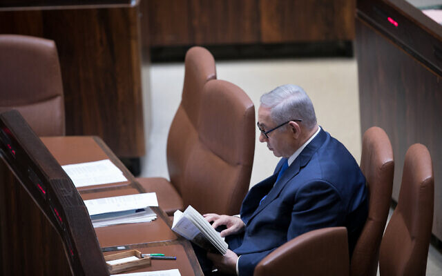 Then-prime minister Benjamin Netanyahu reads a book during a Knesset plenum session on March 12, 2018. (Miriam Alster/Flash90)