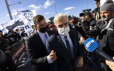 Foreign Affairs Minister Yair Lapid walks through a protest supporting the establishment of a committee of inquiry into the submarine affair, outside the Prime Minister's Office in Jerusalem, January 23, 2022. (Olivier Fitoussi/Flash90)
