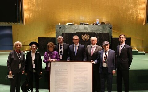 Israel's Ambassador to the UN Gilad Erdan holds an enlarged copy of the resolution passed on January 20, 2022 to combat Holocaust denial, flanked by Holocaust survivors at the General Assembly. (Israel's Mission to the UN)