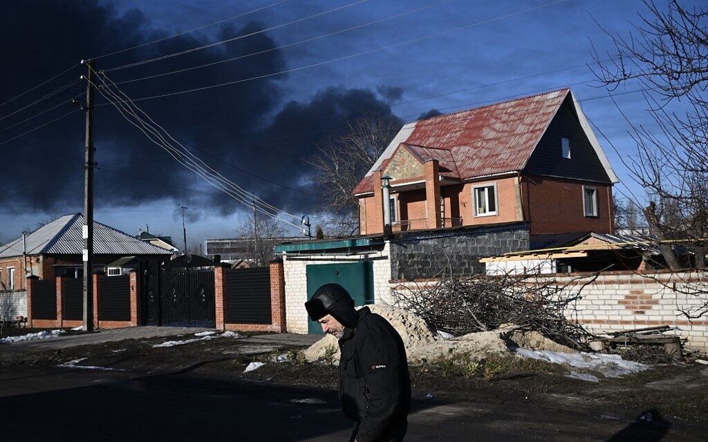 A man walks in a street as black smoke rises from a military airport in Chuguyev near Kharkiv on February 24, 2022 (Aris Messinis / AFP)
