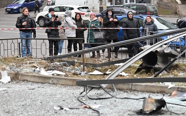 People react standing behind the cordoned off area around the remains of a shell in Kyiv on February 24, 2022 (Sergei SUPINSKY / AFP)