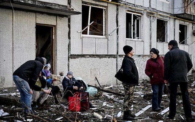 People stand outside a destroyed building after bombings on the eastern Ukraine town of Chuguiv on February 24, 2022 (Aris Messinis / AFP)