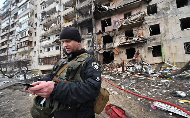 A police officer stands guard at a damaged residential building at Koshytsa Street, on the outskirts of the Ukrainian capital Kyiv, where a military shell allegedly hit, on February 25, 2022. (Genya Savilov/AFP)