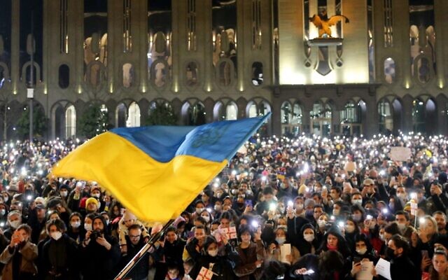 Demonstrators hold their smartphones with torches lit as a Ukranian flag is waved during a rally in support of Ukraine, in Tbilisi on February 25, 2022. (Vano Shlamov / AFP)