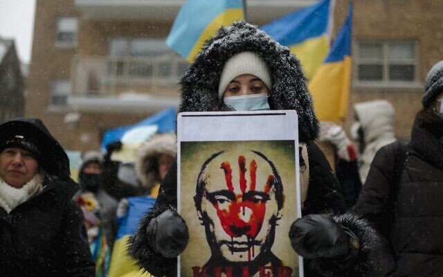 A woman holds a portrait of Russian president Vladimir Putin with a bloody hand on his face as members of the Ukrainian community protest in front of the Consulate General of the Russian Federation on in Montreal, Quebec, February 25, 2022. (Andrej Ivanov / AFP)
