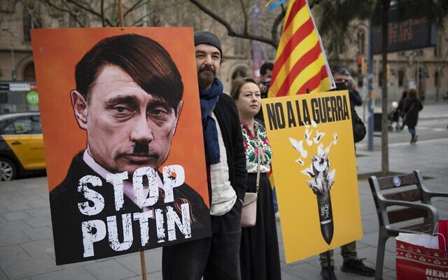 A demonstrator holds a sign depicting the Russian president as Adolf Hitler and reading 'Stop Putin' during a protest against Russia's military operation in Ukraine, in Barcelona on February 26, 2022. (Josep LAGO / AFP)