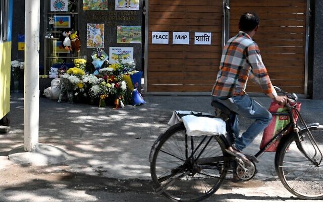 A cyclist peddles past the main gate of the Ukrainian embassy where flowers, soft toys and posters are placed as a sign of support in New Delhi on February 27, 2022. (Money SHARMA / AFP)