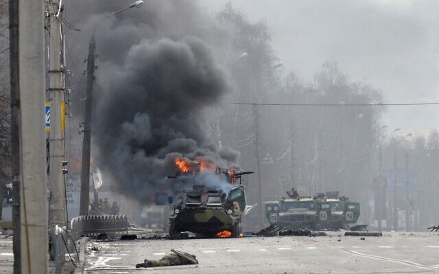 This photograph, taken on February 27, 2022, shows a Russian Armoured personnel carrier (APC) burning next to an unidentified soldier's body during a fight with the Ukrainian armed forces in Kharkiv. (Sergey Bobok/AFP)