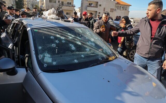 Palestinians inspect a bullet-riddled car belonging to three Palestinian terror suspects killed by Israeli forces in the West Bank city of Nablus, February 8, 2022. (Jaafar Ashtiyeh/AFP)