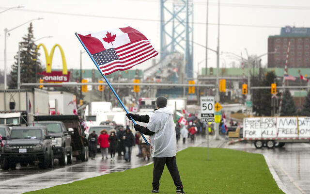 A man waves a Canadian and American flag as truckers and supporters block the access leading from the Ambassador Bridge, linking Detroit and Windsor, as truckers and their supporters continue to protest against COVID-19 vaccine mandates and restrictions, in Windsor, Ontario, February 11, 2022. (Nathan Denette/The Canadian Press via AP)