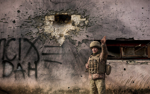 A Ukrainian serviceman points to the direction of the incoming shelling next to a building which was hit by a large caliber mortar shell in the frontline village of Krymske, Luhansk region, in eastern Ukraine, Feb. 19, 2022 (AP Photo/Vadim Ghirda)