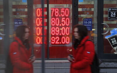 A woman walks by an exchange office screen showing the currency exchange rates of US Dollar and Euro to Russian Rublesin Moscow, on February 22, 2022. (AP Photo/Alexander Zemlianichenko Jr)