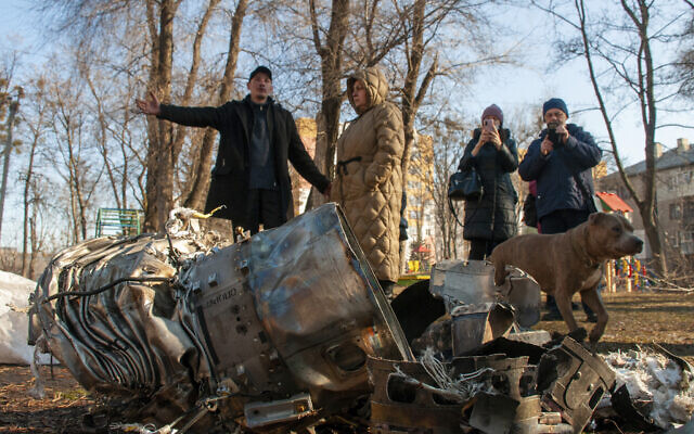 People stand next to fragments of military equipment on the street in the aftermath of an apparent Russian strike in Kharkiv in Kharkiv, Ukraine, Feb. 24, 2022. (Andrew Marienko/AP)