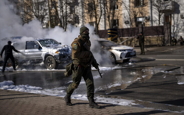Ukrainian soldiers take positions outside a military facility as two cars burn, in a street in Kyiv, Ukraine, on February 26, 2022. (Emilio Morenatti/AP)