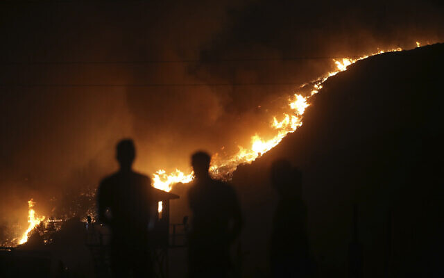 People stand in front of Kemerkoy Thermal Power Plant with a blaze from a wildfire approaching in the background, in Milas, Mugla, Turkey, Aug. 3, 2021. A panel of scientists convened by the UN has published a report on the impacts of climate change on the planet, including on the natural world and human civilization. (AP Photo/Emre Tazegul, File)