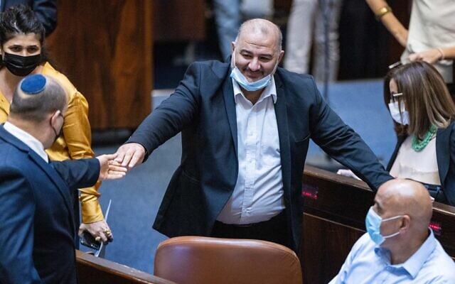 Ra'am party head, Mansour Abbas (c), grasps the hand of prime minister Naftali Bennett in the Knesset in Jerusalem, on October13, 2021. (Yonatan Sindel/Flash90)