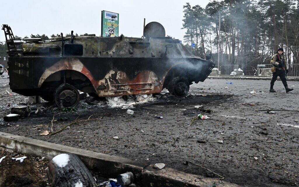 An armed man walks past a burned armored personnel carrier (APC) BTR-4 on a check-point in the city of Brovary outside Kyiv on March 1, 2022. (Genya Savilov/AFP)
