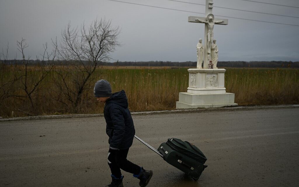 A boy fleeing the conflict in Ukraine walks past a crucifix with a suitcase after crossing the Moldova-Ukraine border checkpoint near the town of Palanca, on March 2, 2022, seven days after Russia's military invasion of Ukraine. (Nikolay Doychinov/AFP)
