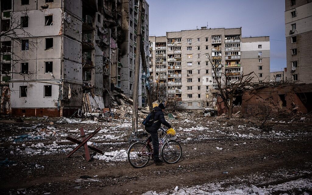 A man rides his bicycle in front of residential buildings damaged in shelling in the city of Chernihiv, on March 4, 2022 (Dimitar Dilkoff/AFP)