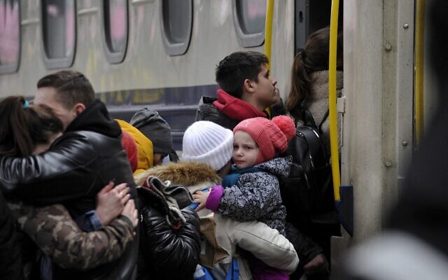 A woman holds a toddler before stepping up in an evacuation train at the central train station in Kyiv on March 6, 2022. (SERGEI CHUZAVKOV / AFP)