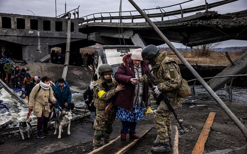 Ukrainian soldiers help an elderly woman to cross a destroyed bridge as she evacuates the city of Irpin, northwest of Kyiv, on March 7, 2022 (Dimitar DILKOFF / AFP)