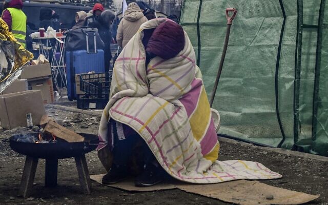 A woman tries to warm herself by a fire due to freezing cold temperatures, after crossing the Ukrainian border into Poland, at the Medyka border crossing in Poland, on March 7, 2022 (Louisa GOULIAMAKI / AFP)
