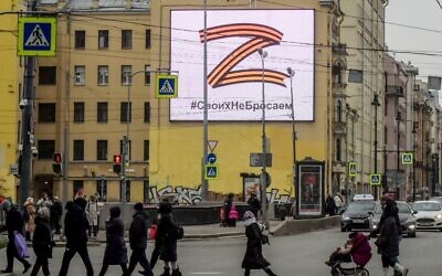 Pedestrians cross a street in front of a billboard displaying the symbol 'Z' in the colors of the ribbon of Saint George and a slogan reading: 'We don't give up on our people,' in support of the Russian armed forces, in Saint Petersburg, on March 7, 2022. (AFP)