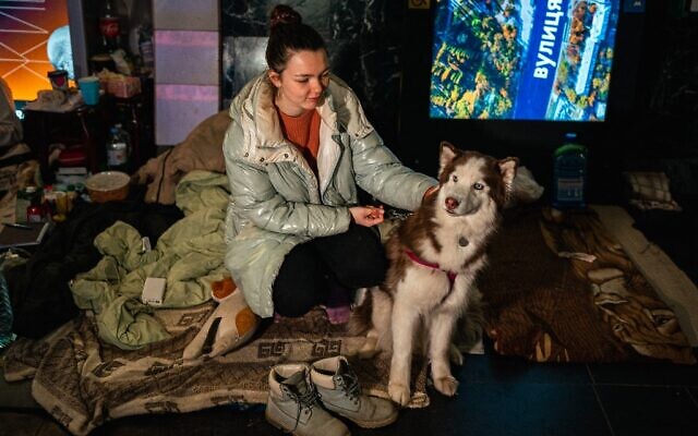 Tania Boyko, 20, and her dog Kari sit on a makeshift bed in a underground metro station used as a bomb shelter in Kyiv on March 8, 2022. (Photo by Dimitar DILKOFF / STF / AFP)