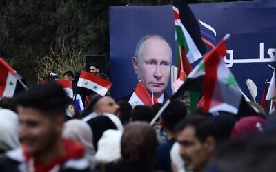 Syrian students wave the Syrian, Russian and Palestinian flags under a billboard bearing the portrait of Russian President Vladimir Putin during a demonstration in support of Russia, following the Russian invasion of Ukraine, at the Aleppo University campus in the Syrian city, March 10, 2022. (Photo by AFP)