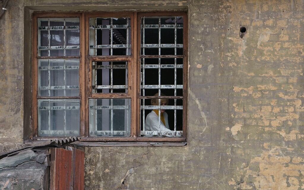 A woman is seen behind the broken window of a residential building damaged in an airstrike in Dnipro, Ukraine on March 11, 2022. (Emre Caylak / AFP)