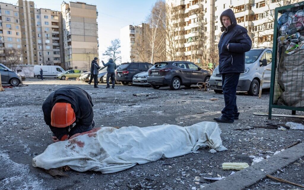 A person mourns next to a covered body near a residential building which was hit by the debris from a downed rocket in Kyiv on March 17, 2022. (Fadel Senna/AFP)