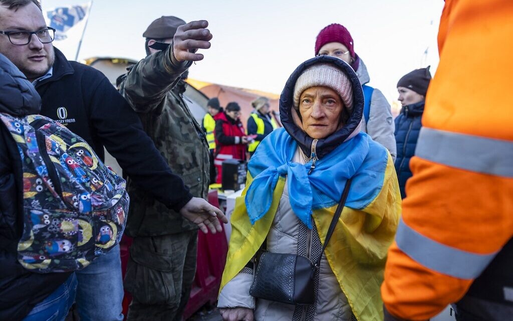 People, including an elderly woman wearing an Ukrainian flag, line up to get into the buses for further transportation at the Medyka Polish-Ukrainian border crossing on March 18, 2022. (Wojtek RADWANSKI / AFP)