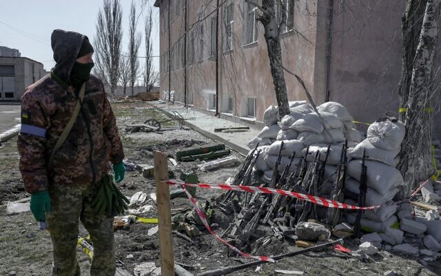 A Ukrainian soldier stands next to rifles of dead and injured troops, close to the military school hit by Russian rockets the day before, in Mykolaiv, southern Ukraine, on March 19, 2022. (Bulent Kilic/AFP)