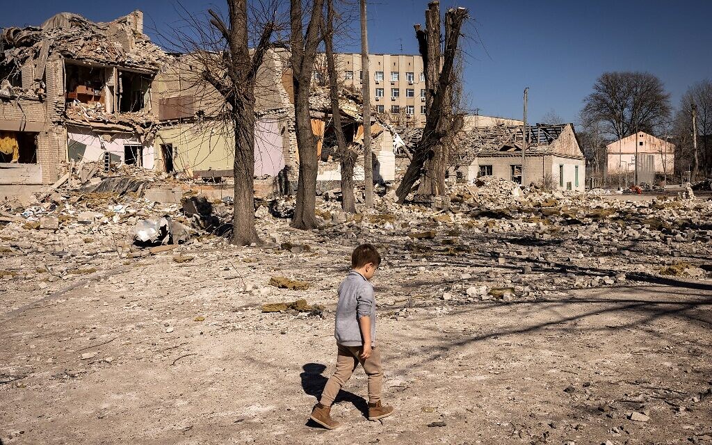 A child walks in front of a damaged school in the city of Zhytomyr, northern Ukraine, on March 23, 2022. (FADEL SENNA / AFP)