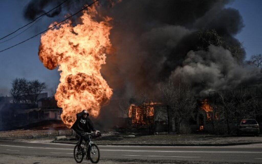 A cyclist rides past flames and smoke rising from a fire following an artillery fire on the 30th day of the invasion of Ukraine by Russian forces in the northeastern city of Kharkiv on March 25, 2022. (Aris Messinis / AFP)