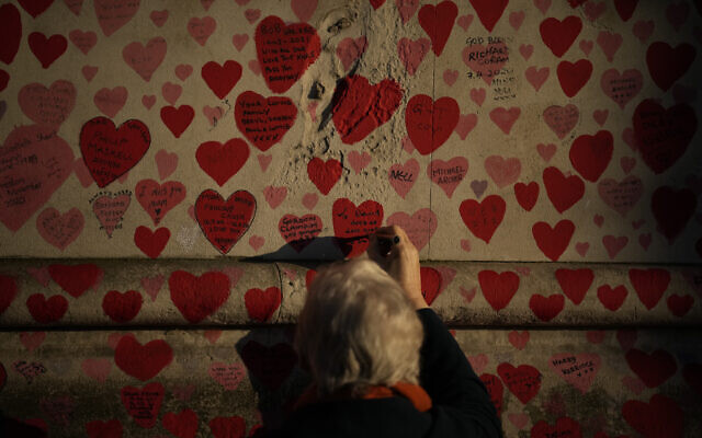 A woman writes a tribute message in a love heart of the National COVID Memorial Wall, in London, Wednesday, Jan. 12, 2022. (AP/Matt Dunham)