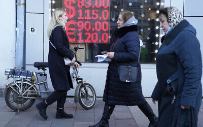 People walk past a currency exchange office screen displaying the exchange rates of US dollar and euro to Russian rubles in Moscow's downtown, Russia, Monday, Feb. 28, 2022. (AP/Pavel Golovkin)