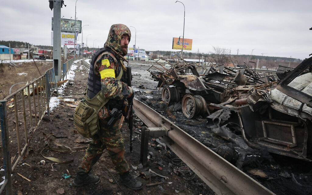 An armed man stands by the remains of a Russian military vehicle in Bucha, close to the capital Kyiv, Ukraine, March 1, 2022. (Serhii Nuzhnenko/AP)