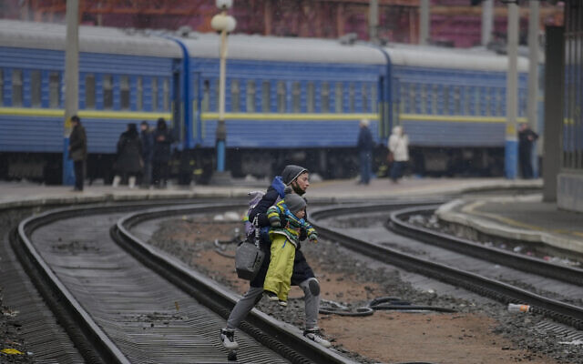 A woman carries a baby over the tracks trying to board a Lviv bound train, in Kyiv, Ukraine, on Thursday, March 3, 2022. (AP Photo/Vadim Ghirda)