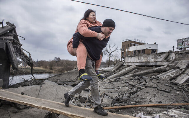 A man carries a woman as they cross an improvised path while fleeing the town of Irpin, Ukraine, Sunday, March 6, 2022. (AP/Oleksandr Ratushniak)