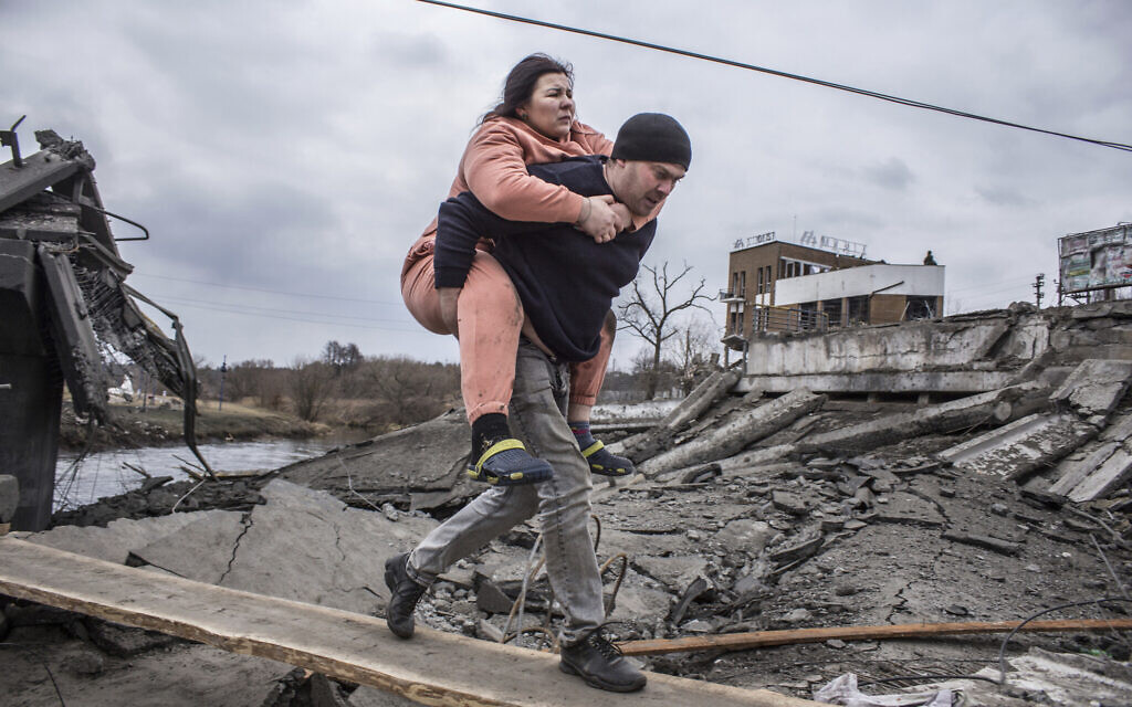 A man carries a woman as they cross an improvised path while fleeing the town of Irpin, Ukraine, March 6, 2022. (AP Photo/Oleksandr Ratushniak)
