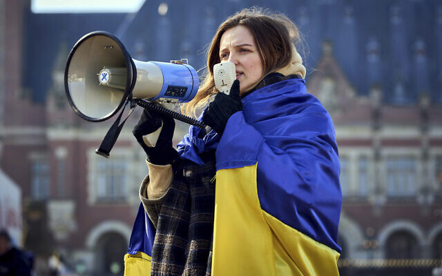 A woman is wrapped in the Ukrainian flag and shouts through a megaphone during a demonstration in front of the International Criminal Court in The Hague, Netherlands, Monday, March 7, 2022. A representative for Kyiv has urged the United Nations' top court to order Russia to halt its devastating invasion of Ukraine, at a hearing snubbed by Russia. (AP Photo/Phil Nijhuis)