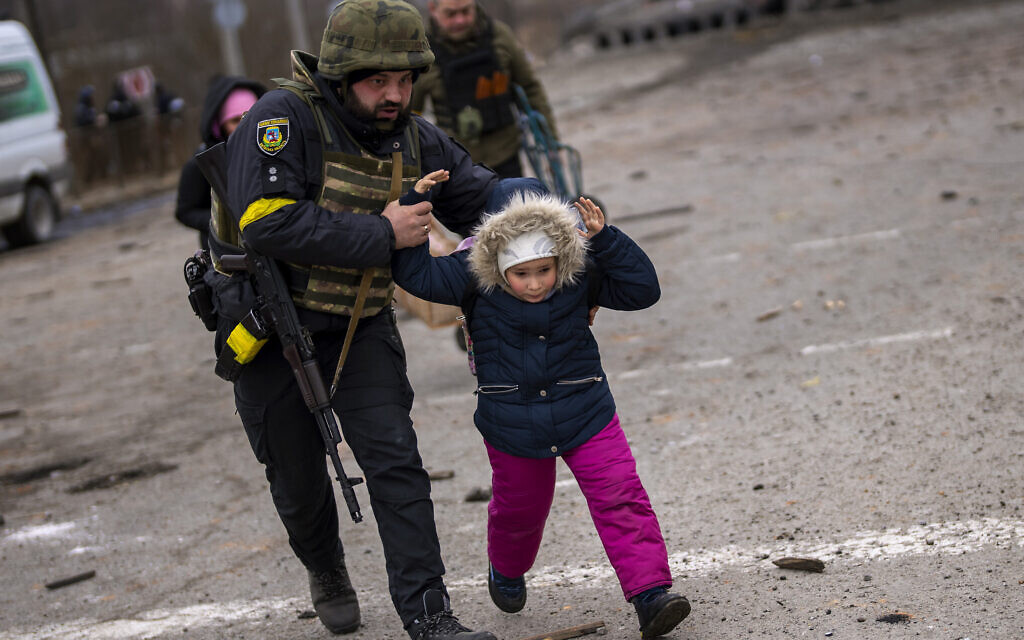 A Ukrainian police officer runs while holding a child as the artillery echoes nearby, while fleeing Irpin on the outskirts of Kyiv, Ukraine, Monday, March 7, 2022. (AP/Emilio Morenatti)
